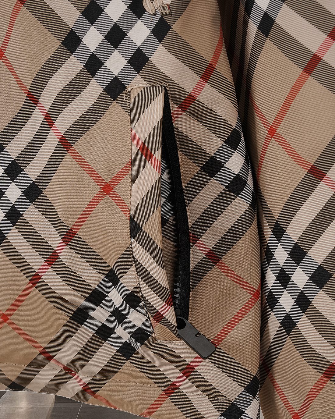 Side seam and zipper guard on beige, black, and red plaid hooded jacket