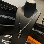 Silver-tone chain necklace with cross charm and snowflake pendant on black display bust