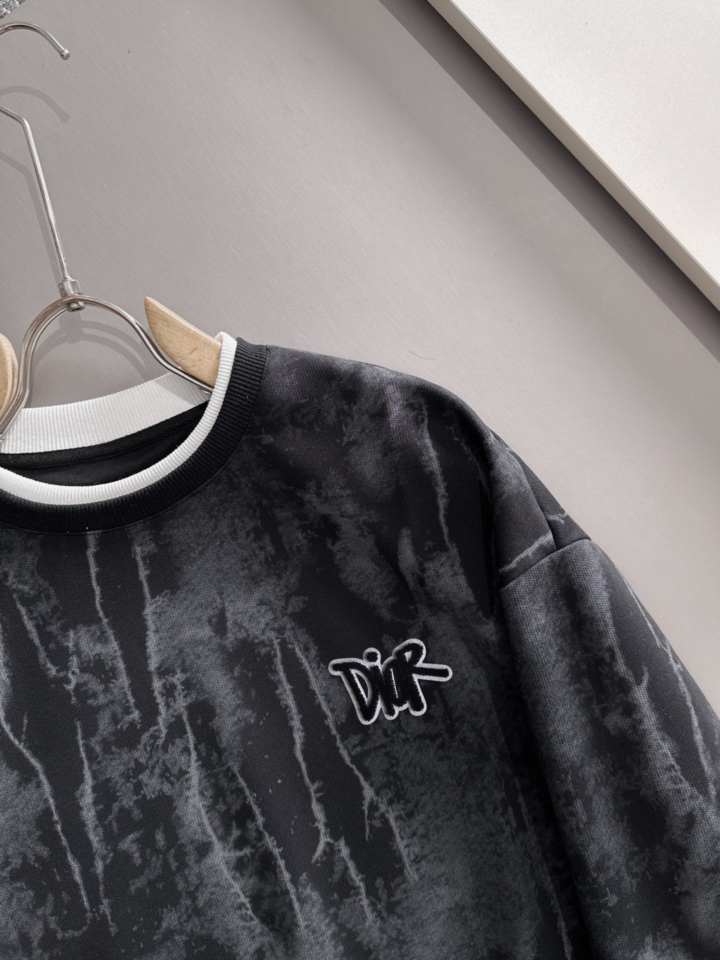 Black sweatshirt close-up: DiR logo with white-and-black ribbed crew collar