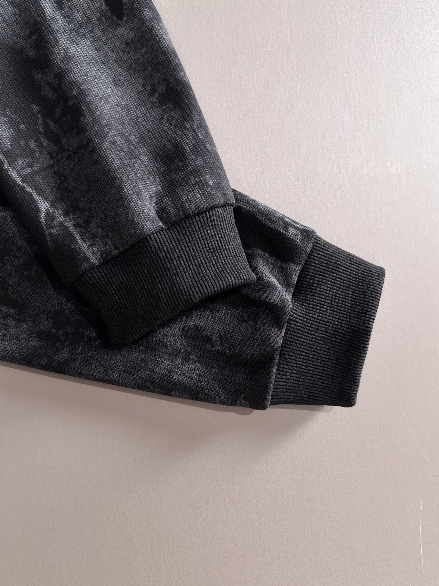 Black sweatshirt sleeve cuff with ribbed knit hem and dark tie-dye fabric texture