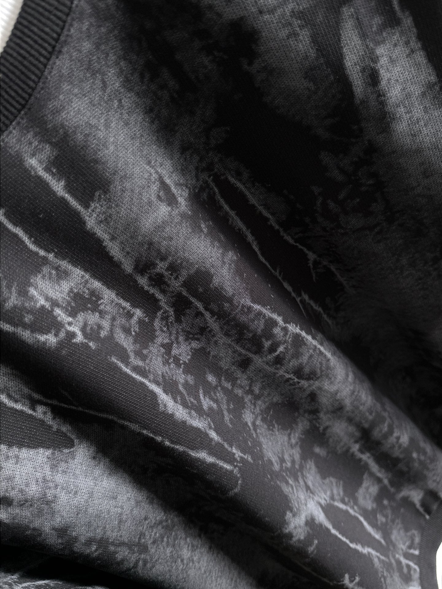 Black long-sleeve sweatshirt fabric close-up with light gray tie-dye streaks