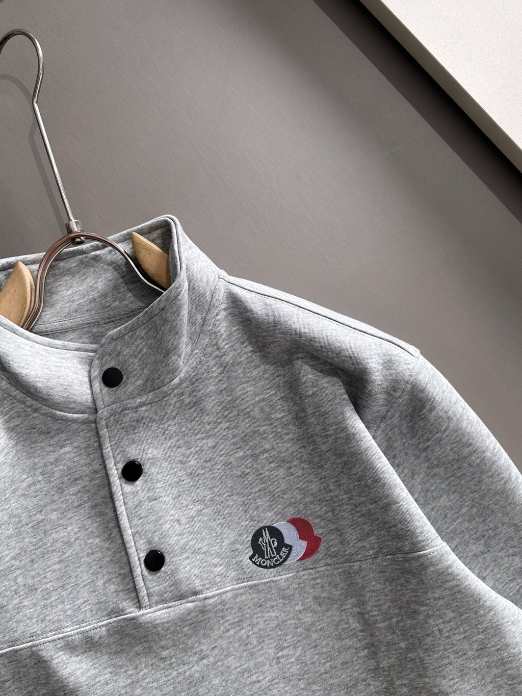 Light gray long-sleeve pullover with stand collar, black buttons, logo patch