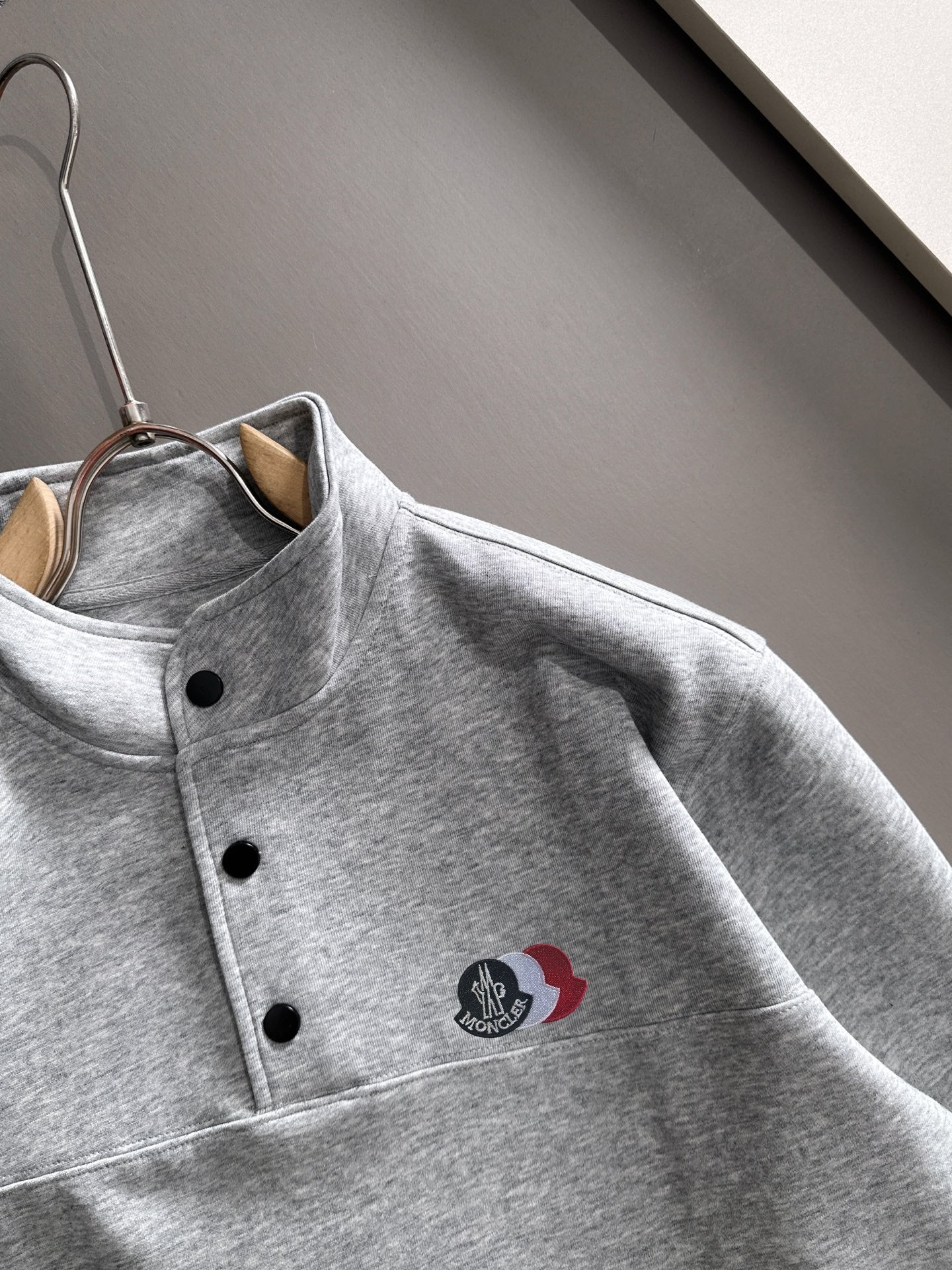Light gray long-sleeve pullover with stand collar, black buttons, logo patch