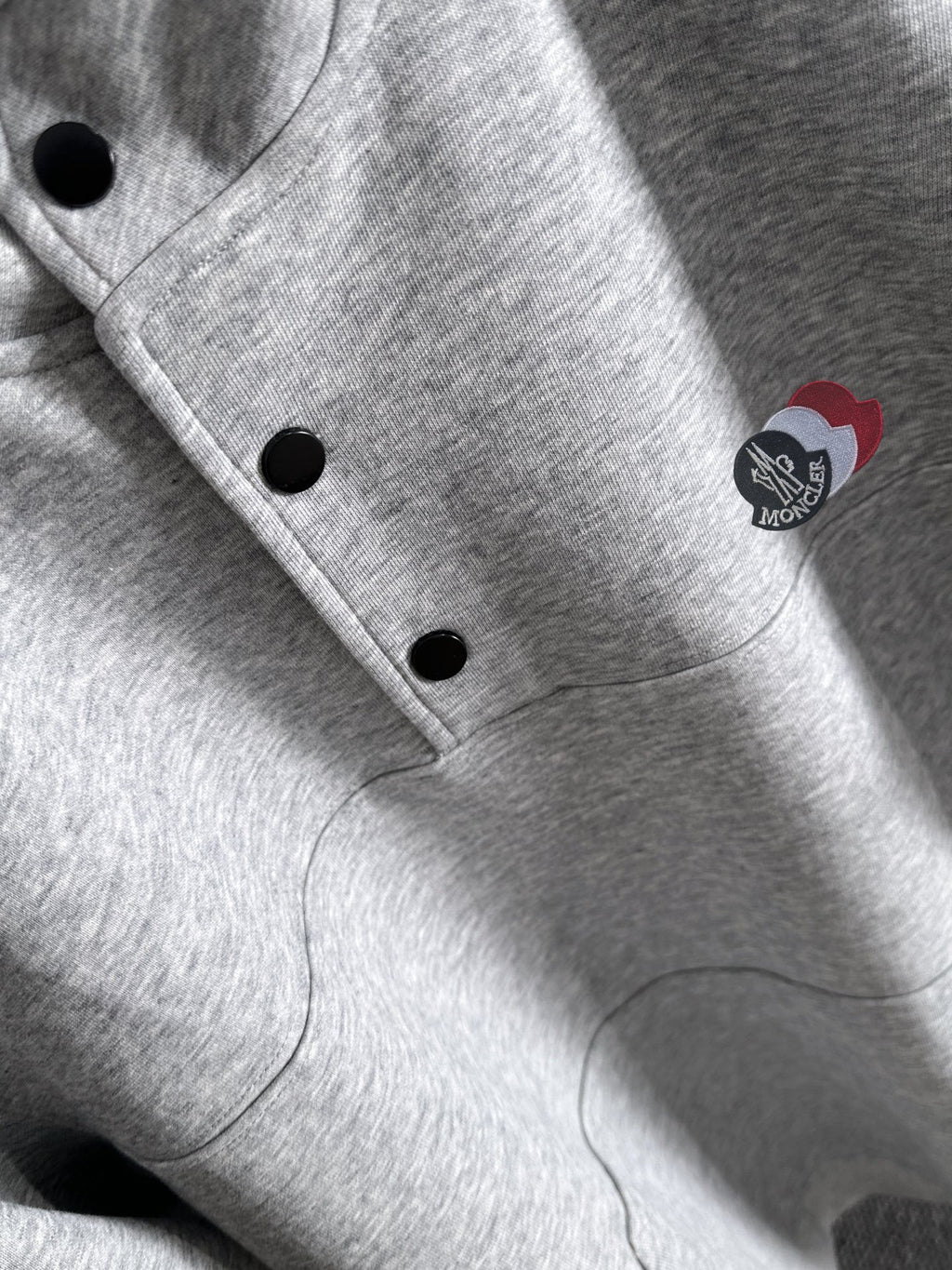 Light gray pullover close-up with black buttons and round logo patch