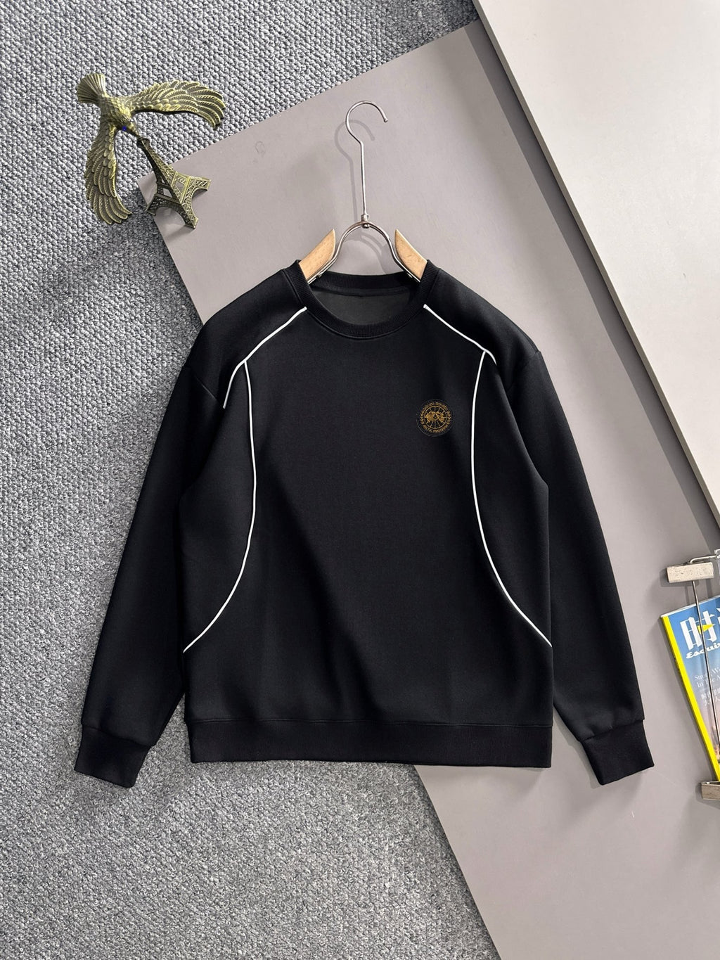 Black long-sleeve sweatshirt with white piping and small gold logo emblem