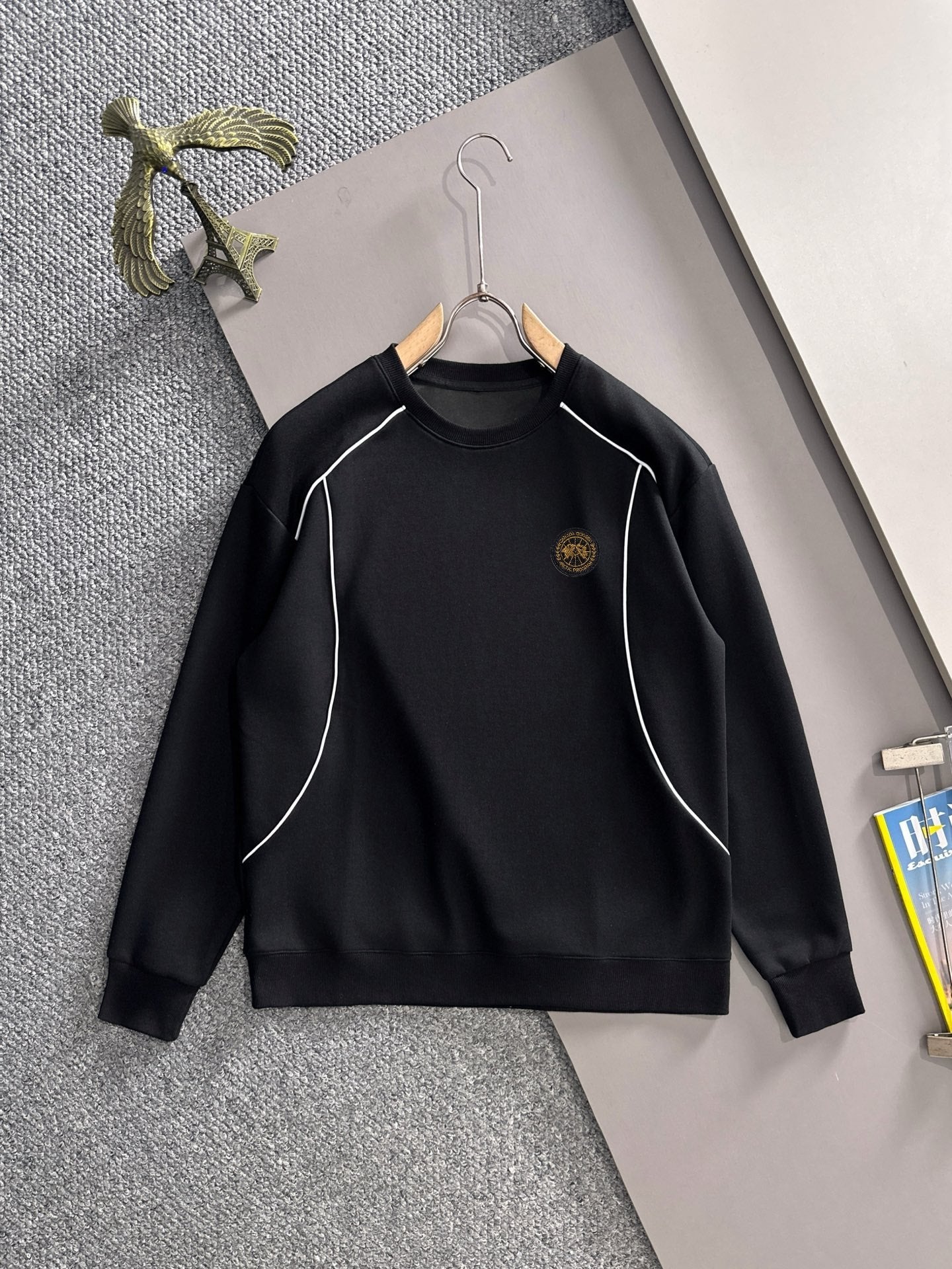 Black long-sleeve sweatshirt with white piping and small gold logo emblem