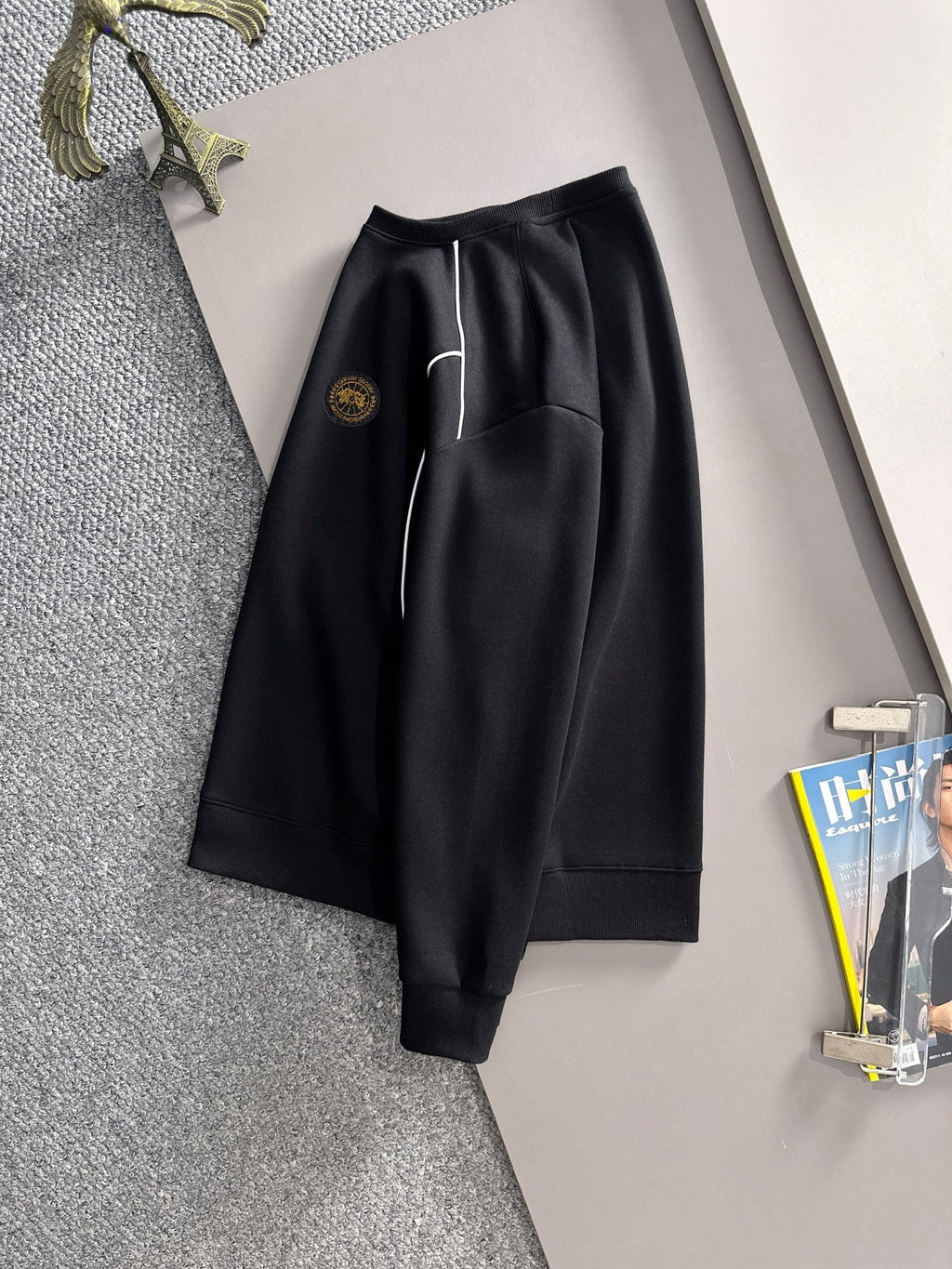 Black track pants with white side stripe and gold logo patch, cuffed hem
