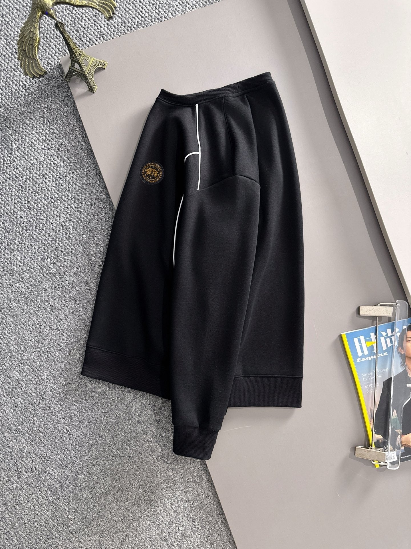 Black track pants with white side stripe and gold logo patch, cuffed hem
