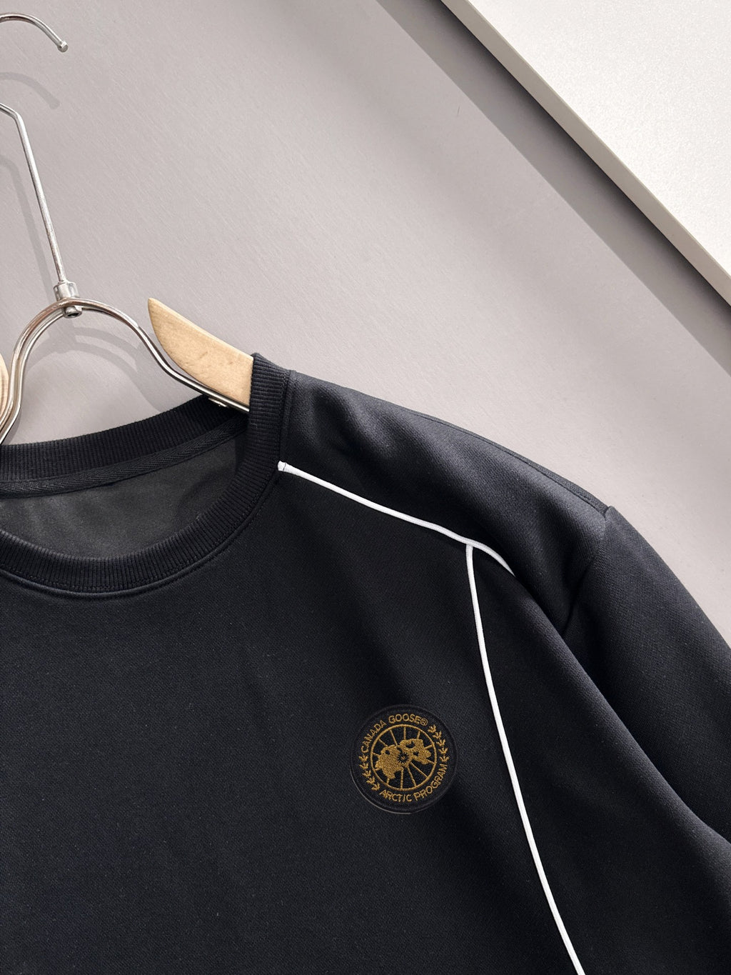 Black crew-neck sweatshirt close-up of gold logo and white side stripe