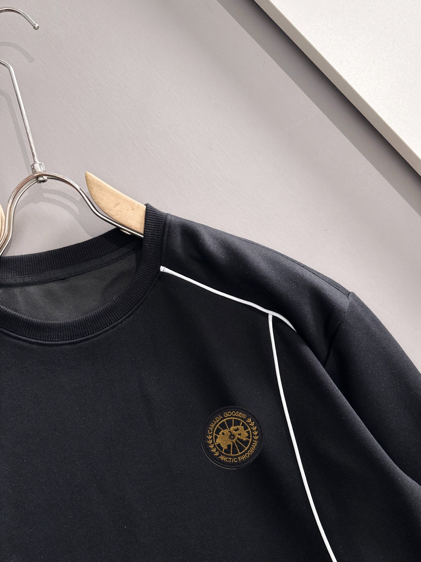 Black crew-neck sweatshirt close-up of gold logo and white side stripe