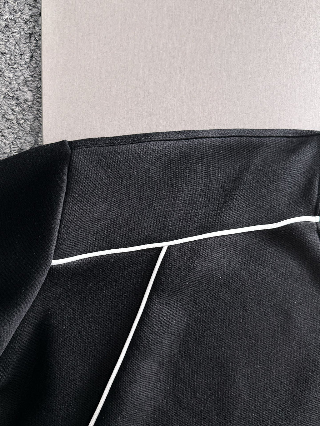 Black sweatshirt panel with white piping trim along the seam