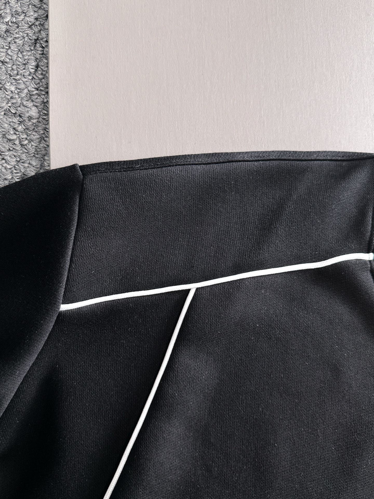 Black sweatshirt panel with white piping trim along the seam