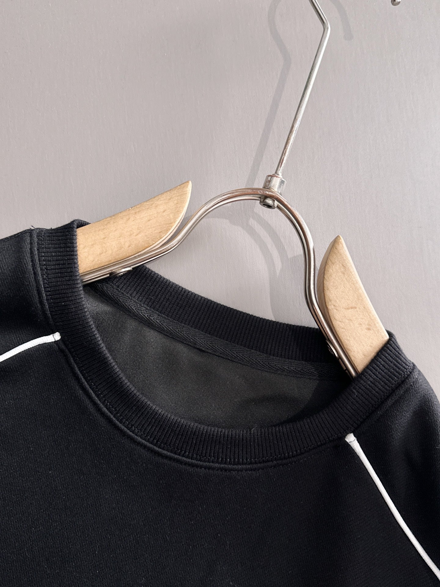 Black crew-neck sweatshirt with white stripe trim on hanger