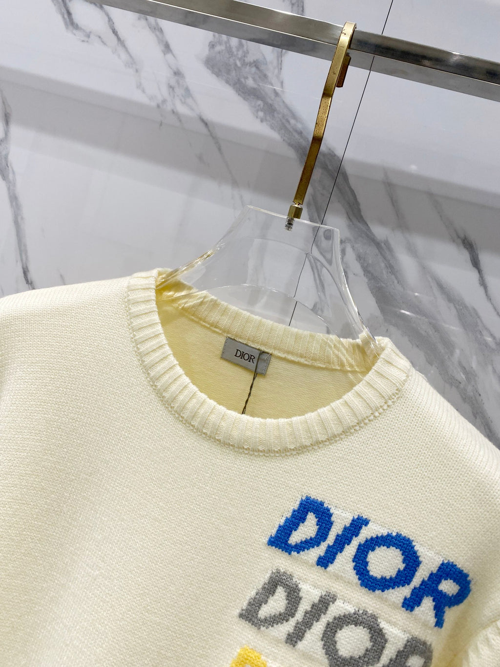 Cream knit sweater close-up of crew neckline and blue multicolor "DIOR" logo text