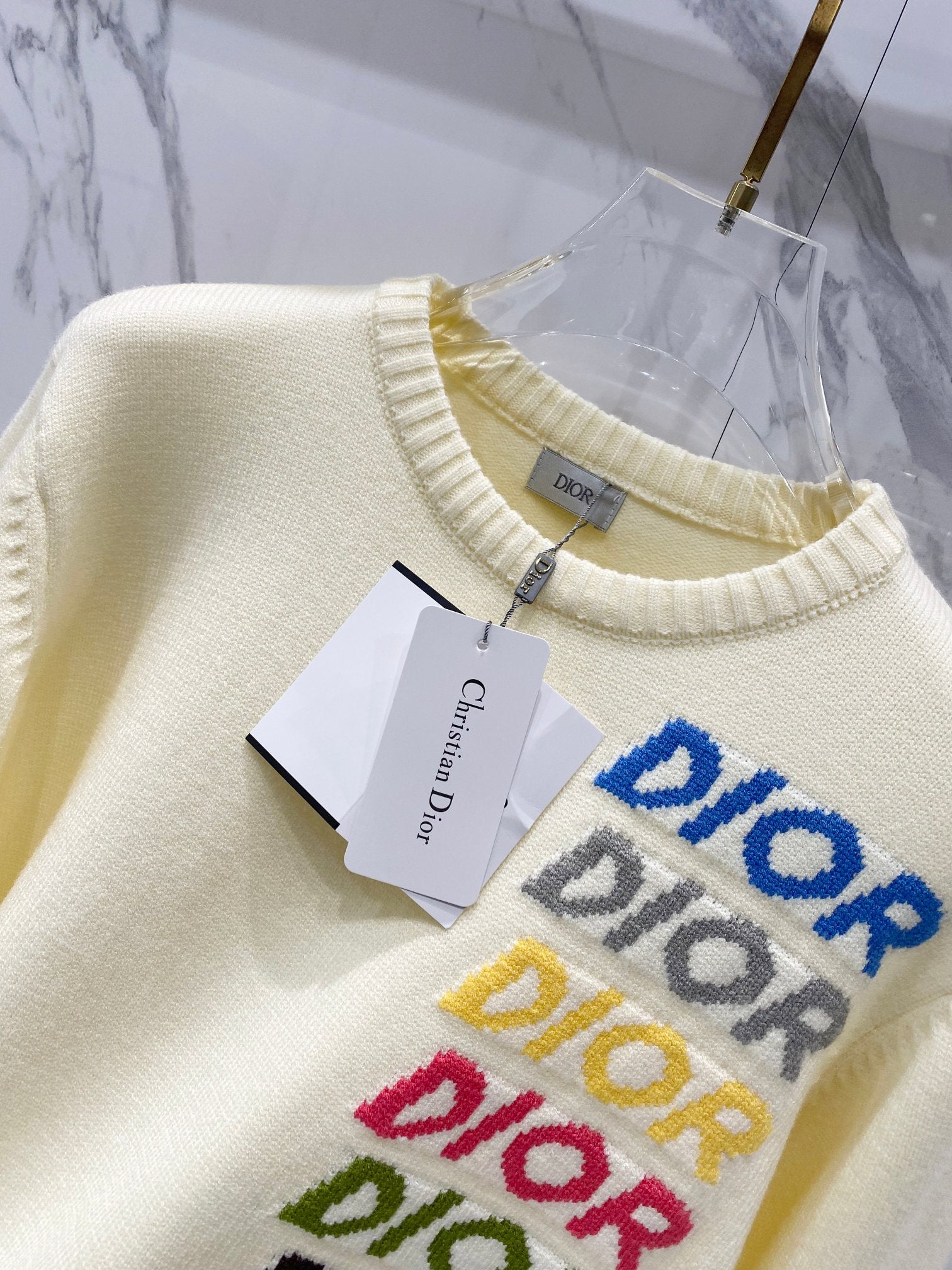 Cream knit sweater front detail with layered logo embroidery and paper tag on chest