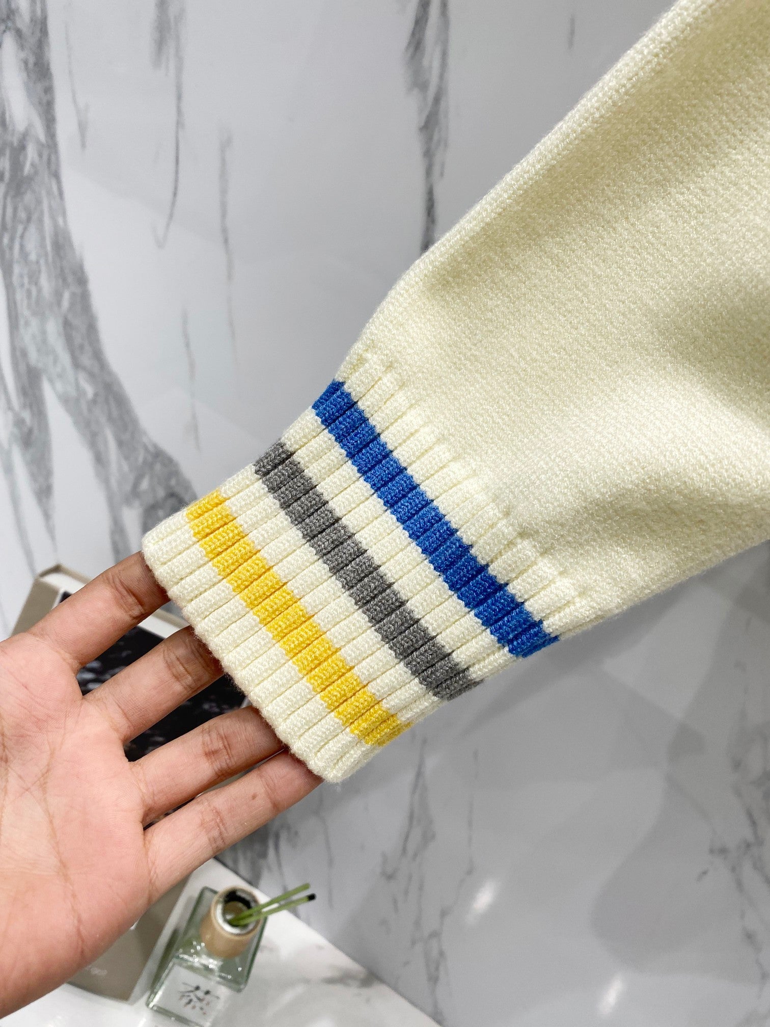 Cream knit sleeve cuff with ribbing and blue, gray, and yellow striped bands