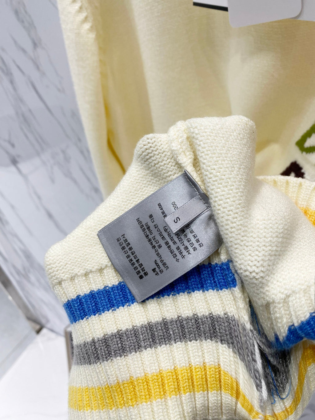 Cream knit cuff with blue, gray, and yellow stripes and attached fabric care tag