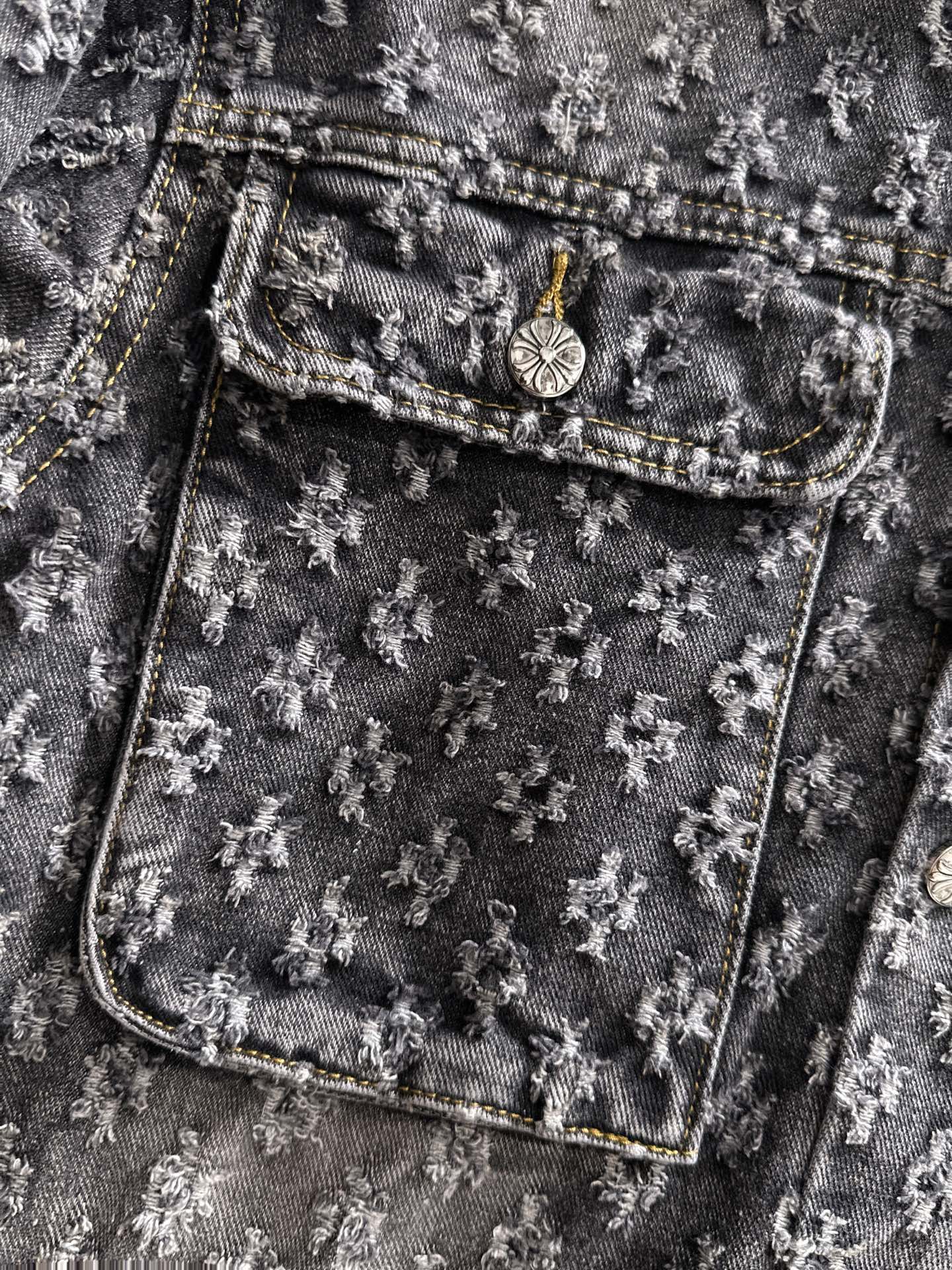 Distressed denim jacket pocket detail with coin-stud emblem and stitched trim