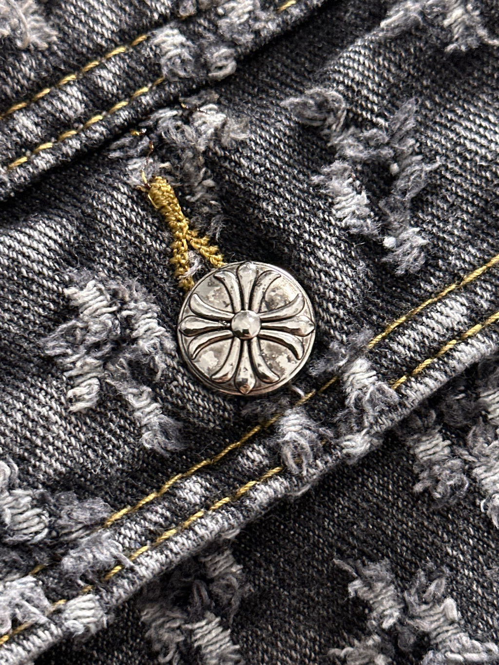 Denim jacket button detail with round engraved emblem and gold stitch accents