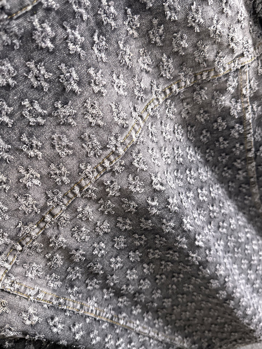Distressed denim jacket fabric close-up with textured embroidery and contrast seam