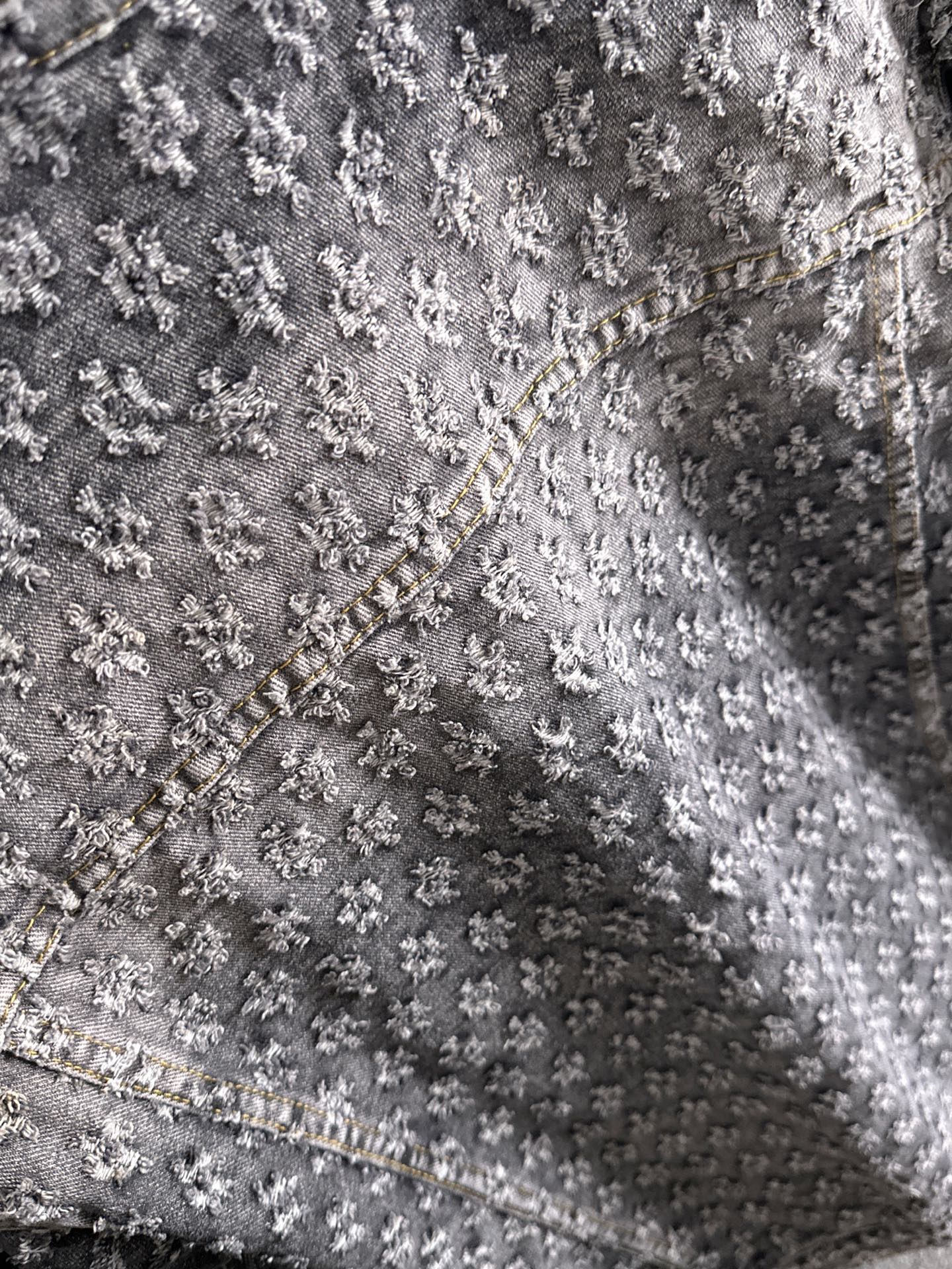 Distressed denim jacket fabric close-up with textured embroidery and contrast seam