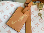 Tan leather luggage tag with cursive monogram logo on monogram canvas