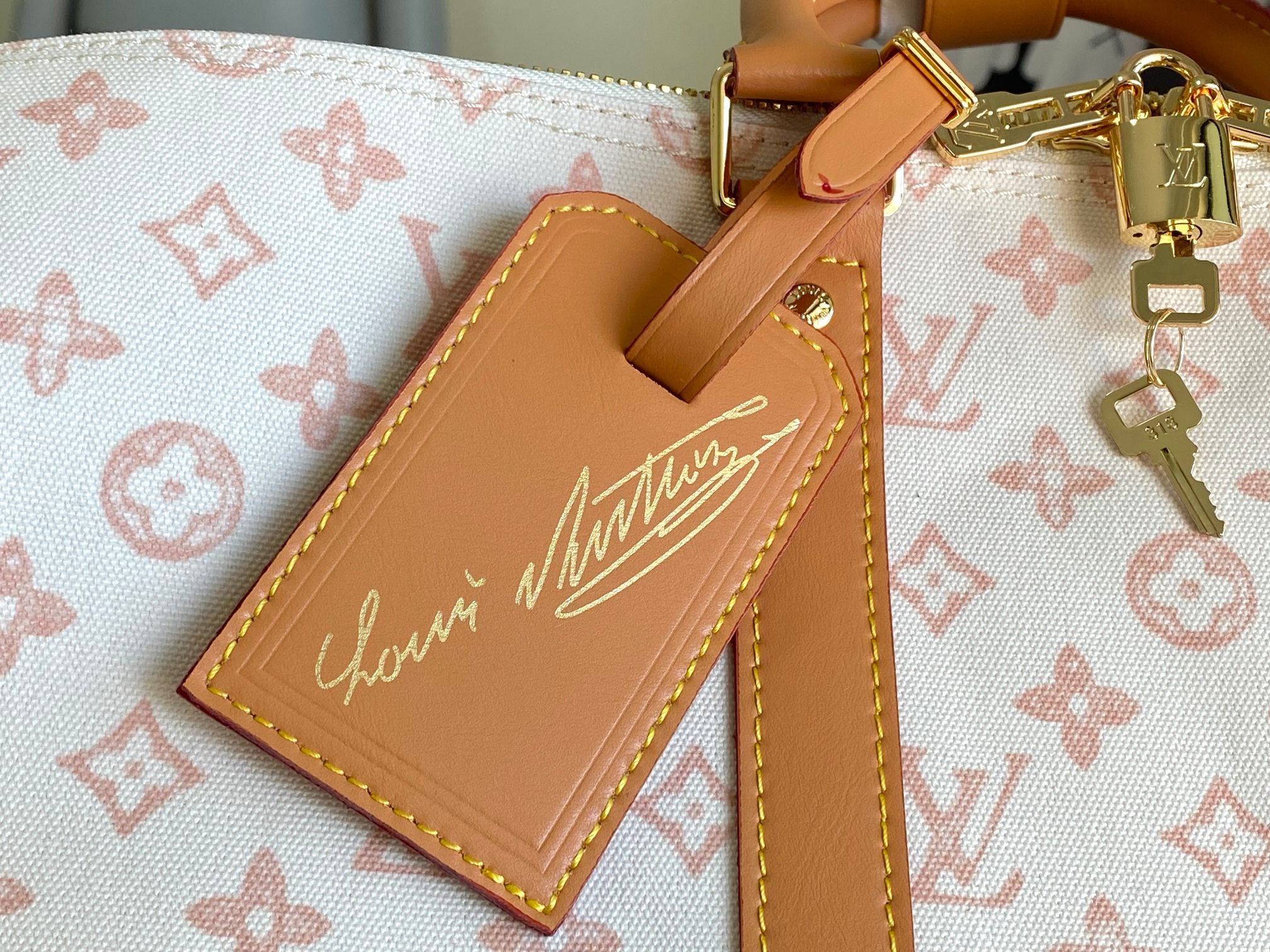 Tan leather luggage tag with cursive monogram logo on monogram canvas