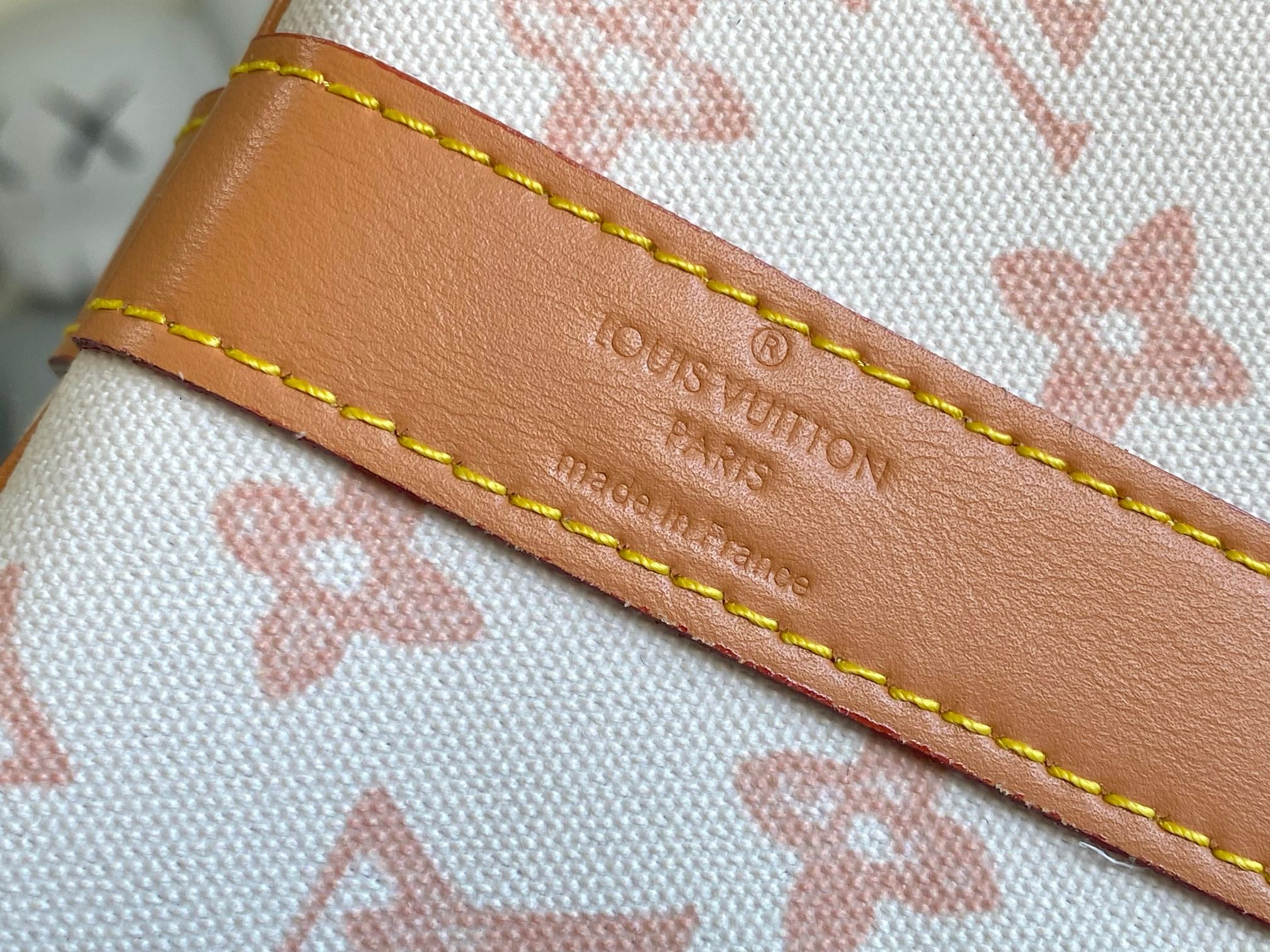 Tan leather label with stitched trim on monogram canvas, embossed text