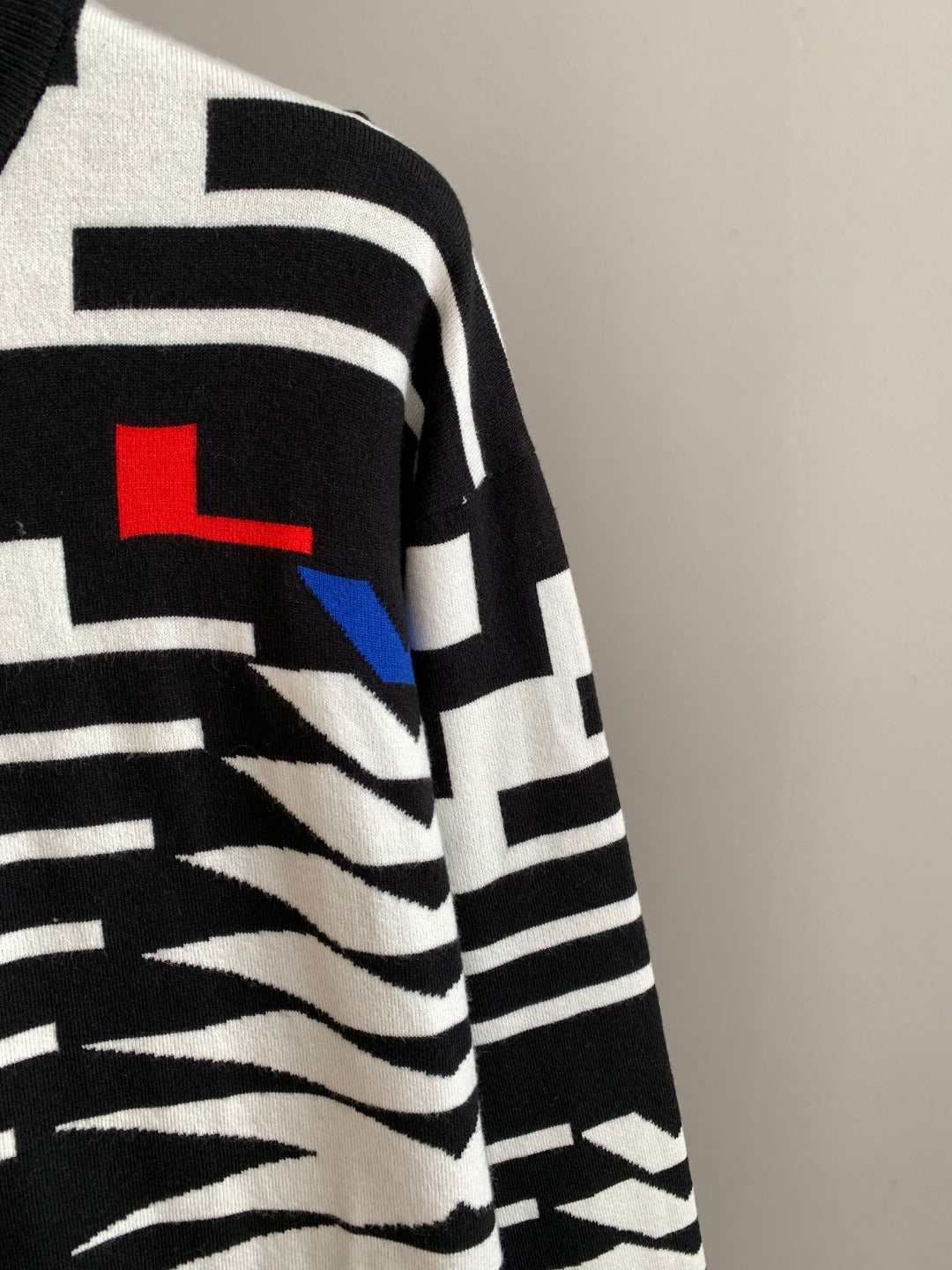 Crewneck sweater sleeve with black and white geometric design and small blue detail