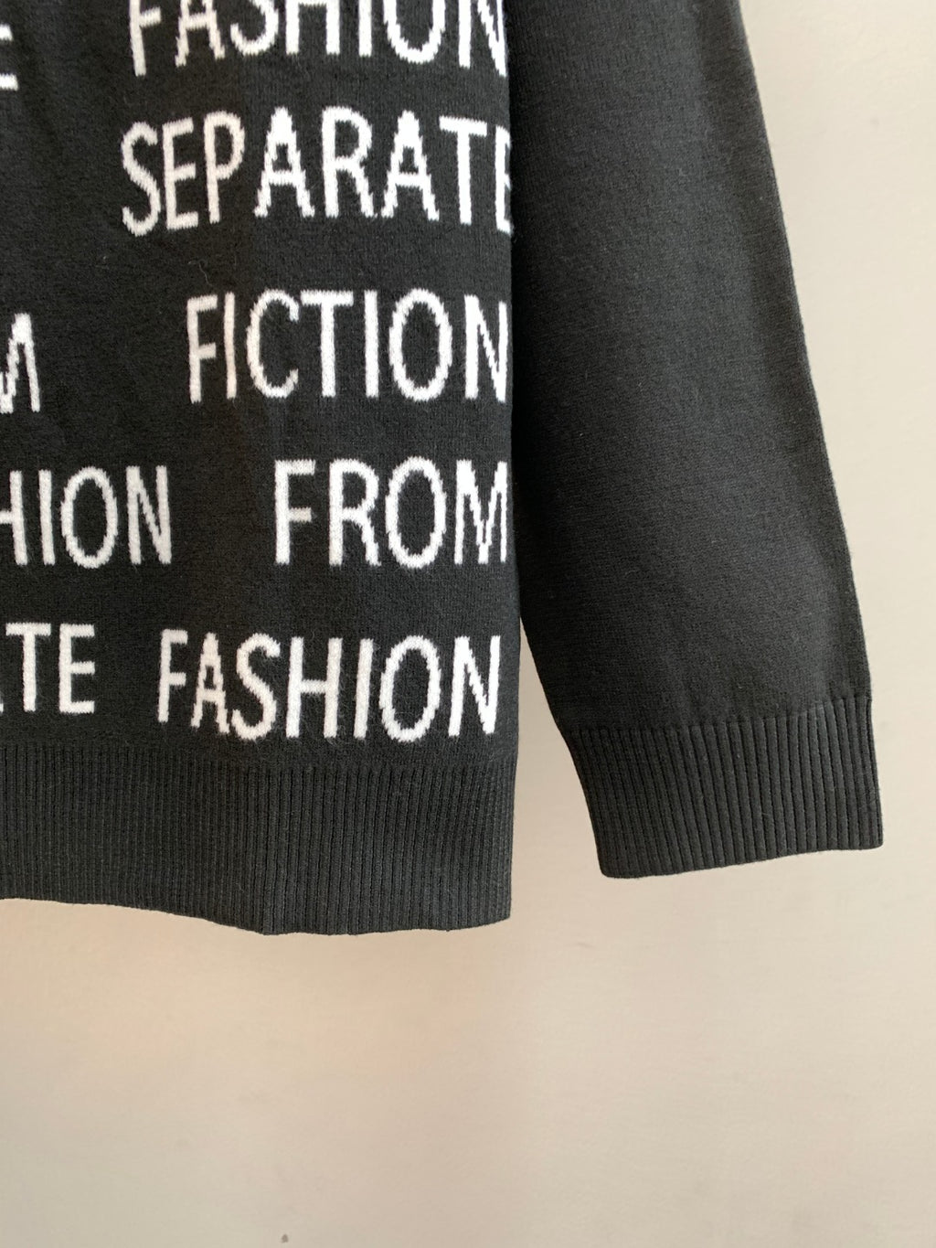 Black long-sleeve sweater with ribbed cuffs and repeating white text print