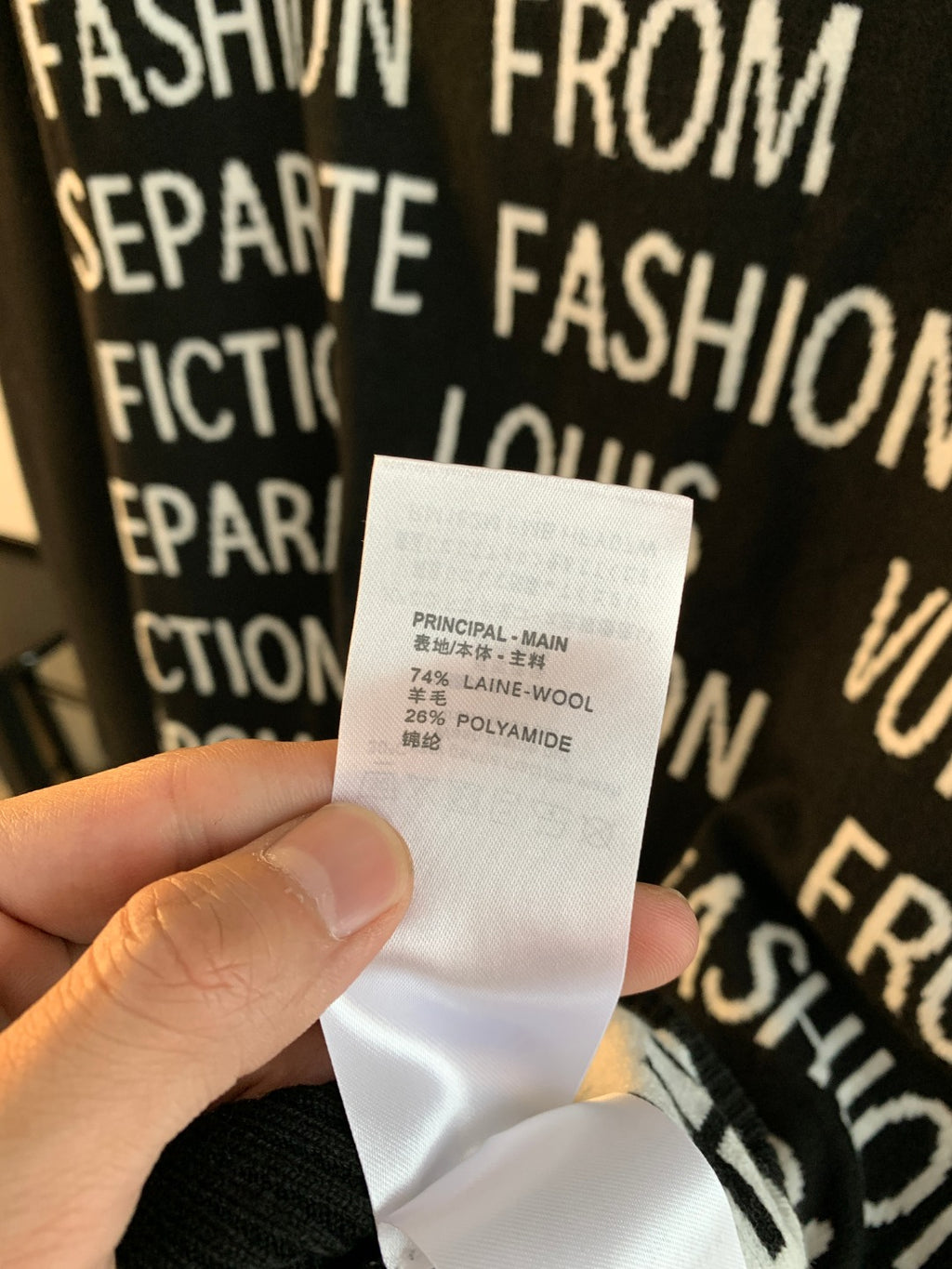 White fabric tag on black sweater showing material "wool" and "polyamide"