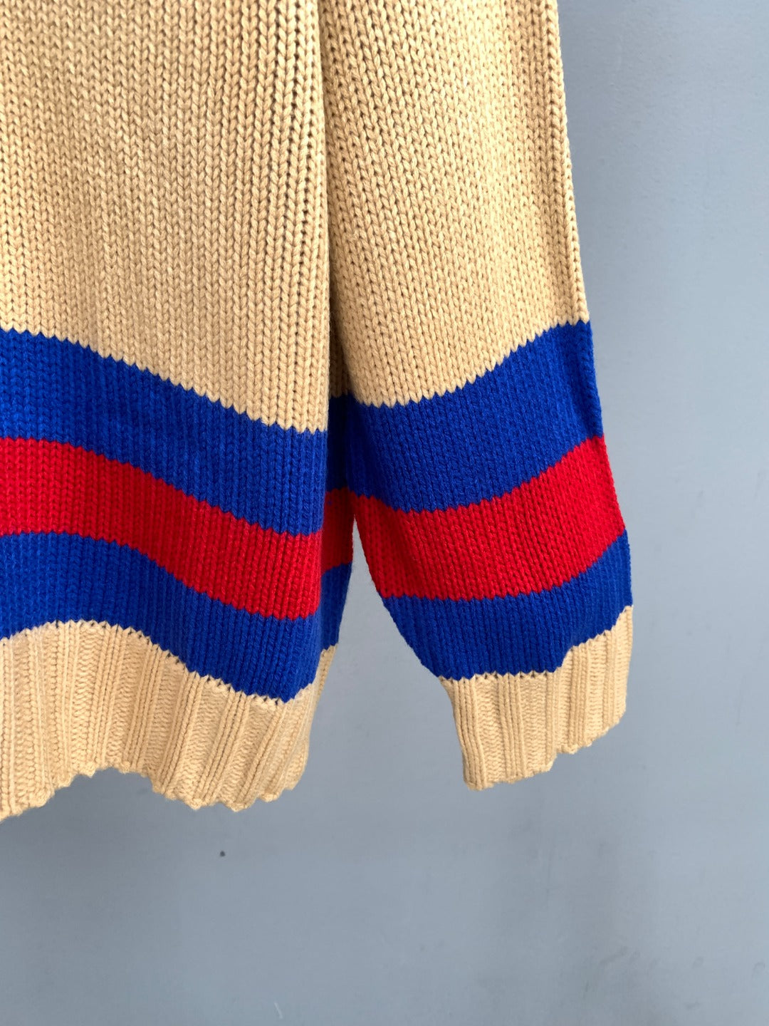 Cream knit sweater sleeve cuff with red and blue horizontal stripes