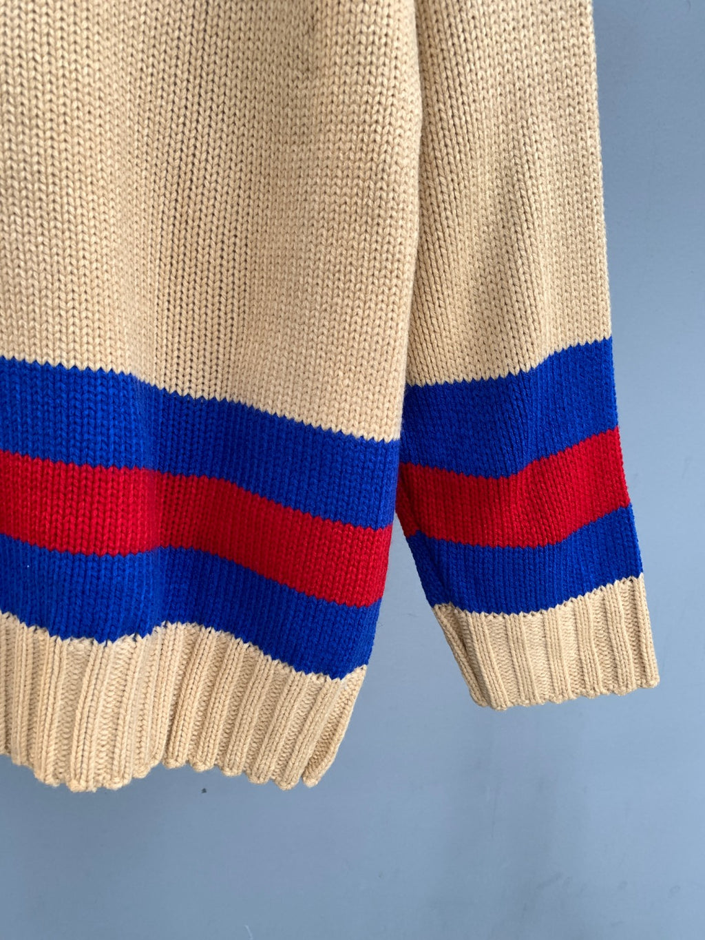 Cream knit sweater cuff with red, blue, and red stripe bands