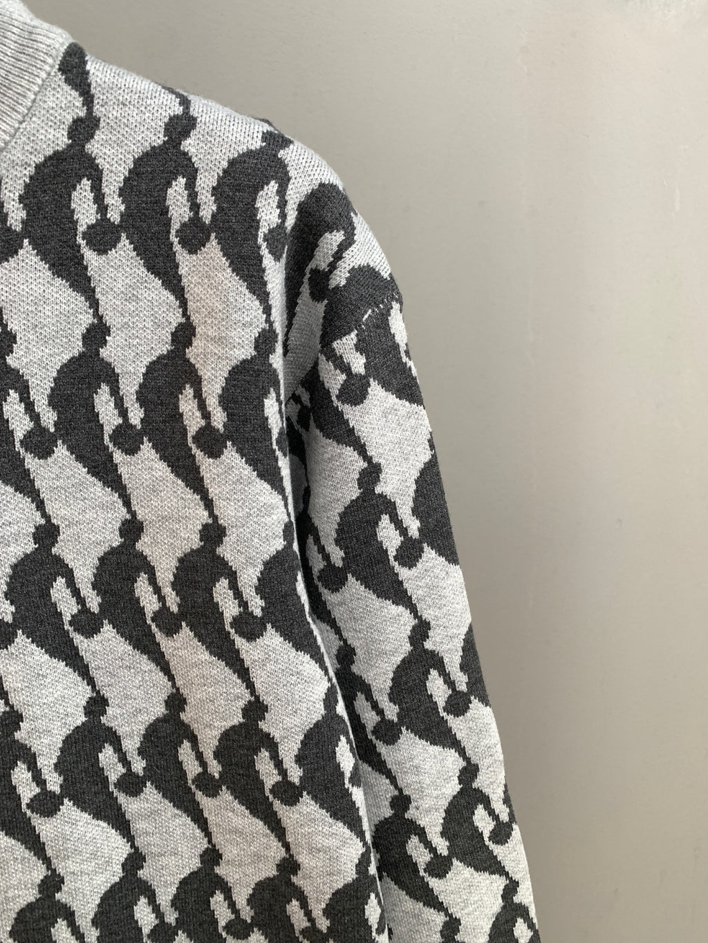 White and black patterned knit sweater sleeve detail, textured knit with repeating silhouettes