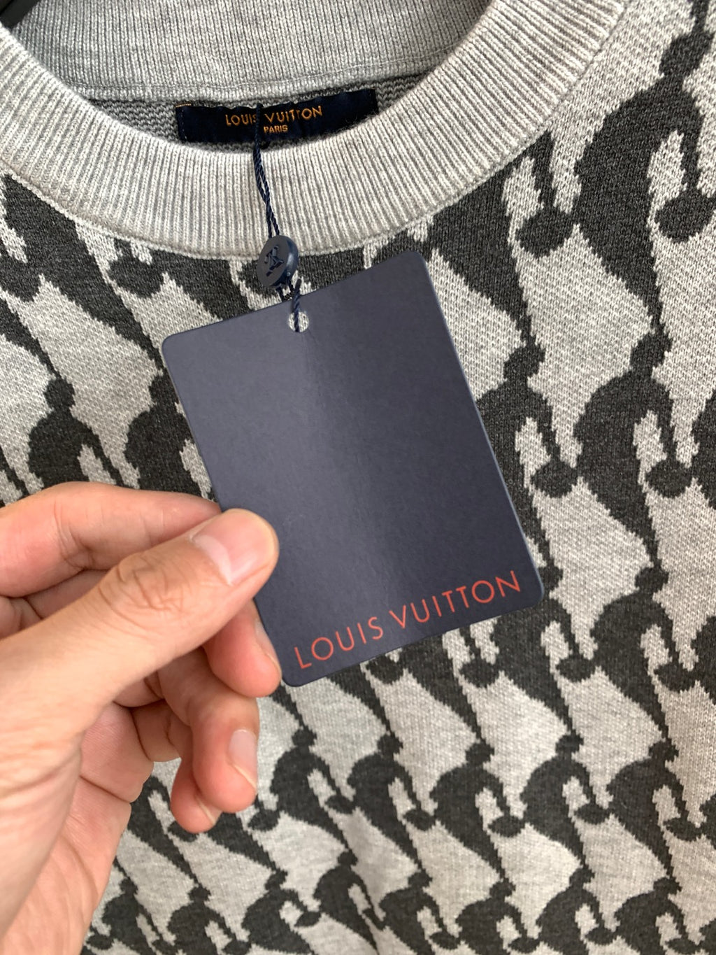 White and black patterned knit sweater with hanging tag held in hand