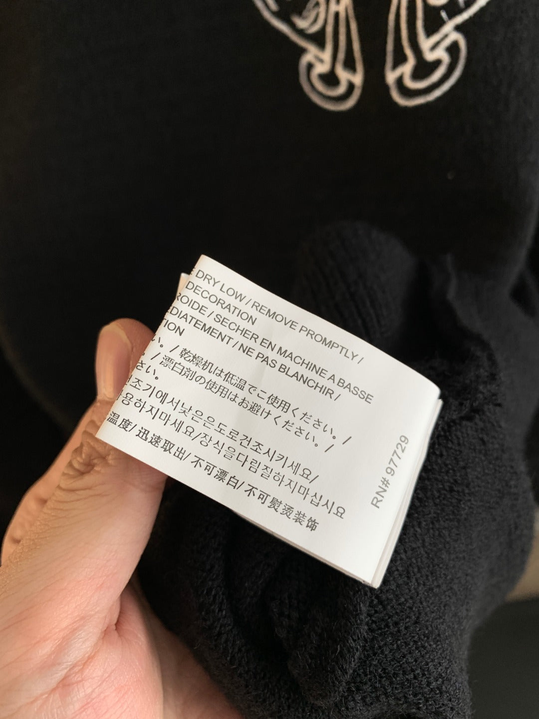 Charcoal sweater care label with printed instructions held near garment