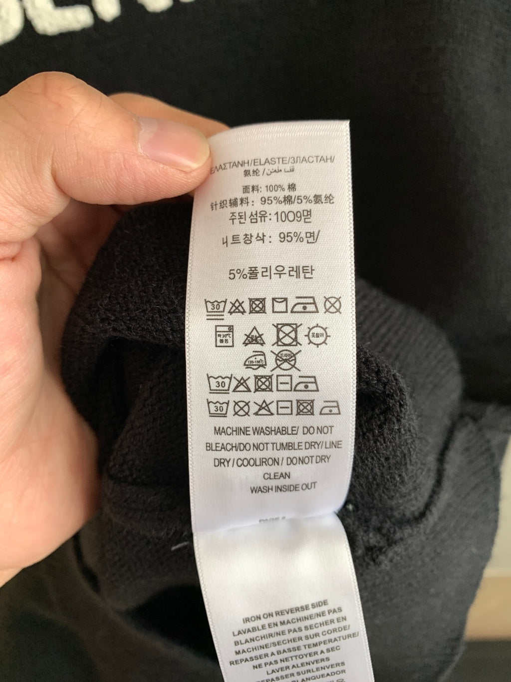 Clothing care label inside dark knit sweater, held in hand