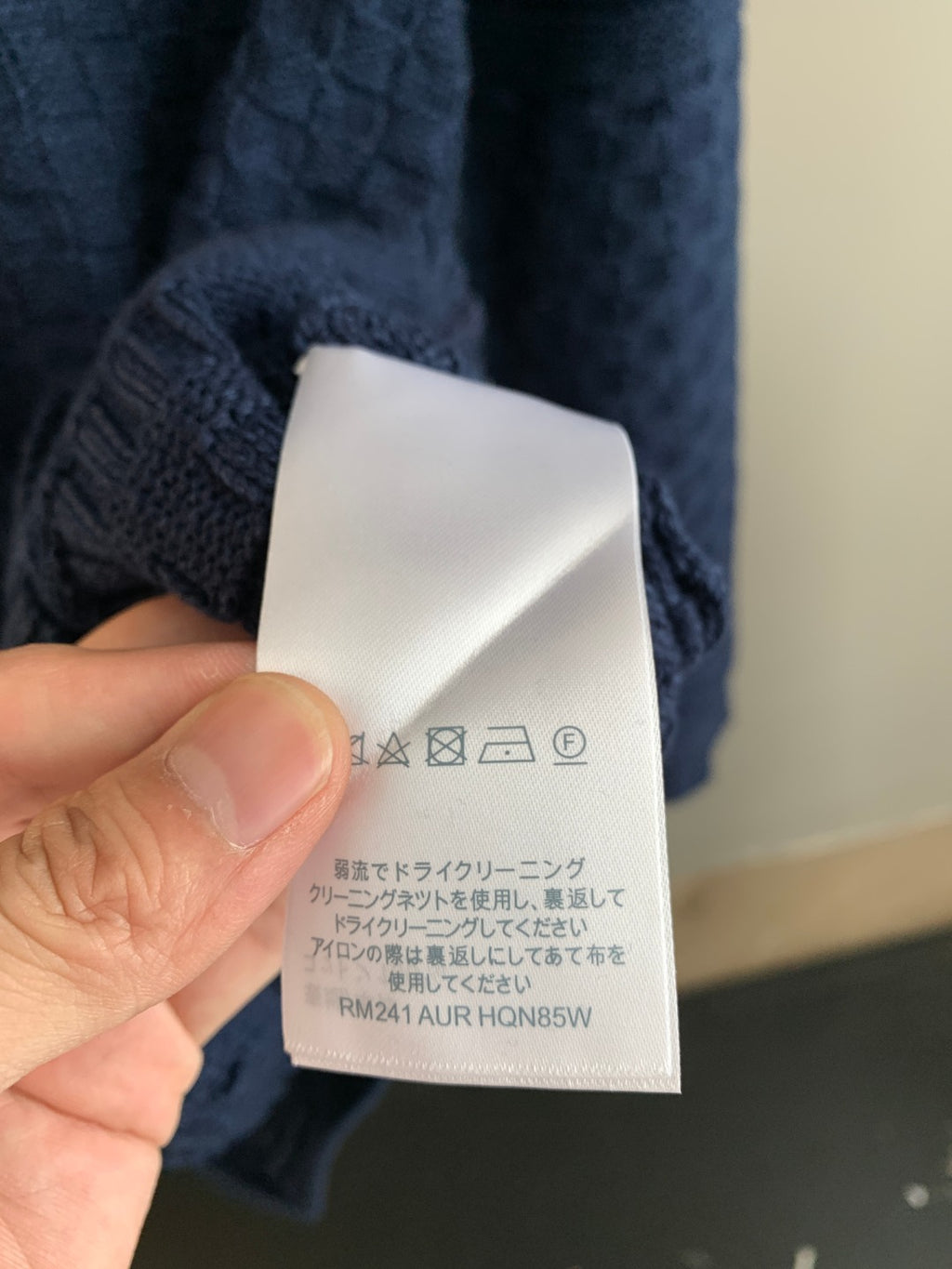 Blue knit sweater care label tag with icon instructions and model code