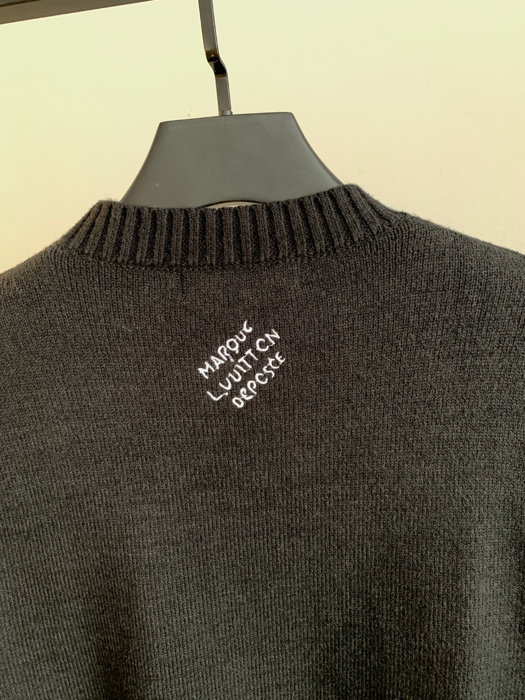 Charcoal knit sweater back with embroidered white text centered