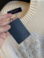 Close-up of cream sweater fabric with Louis Vuitton rhinestone text and brand tag