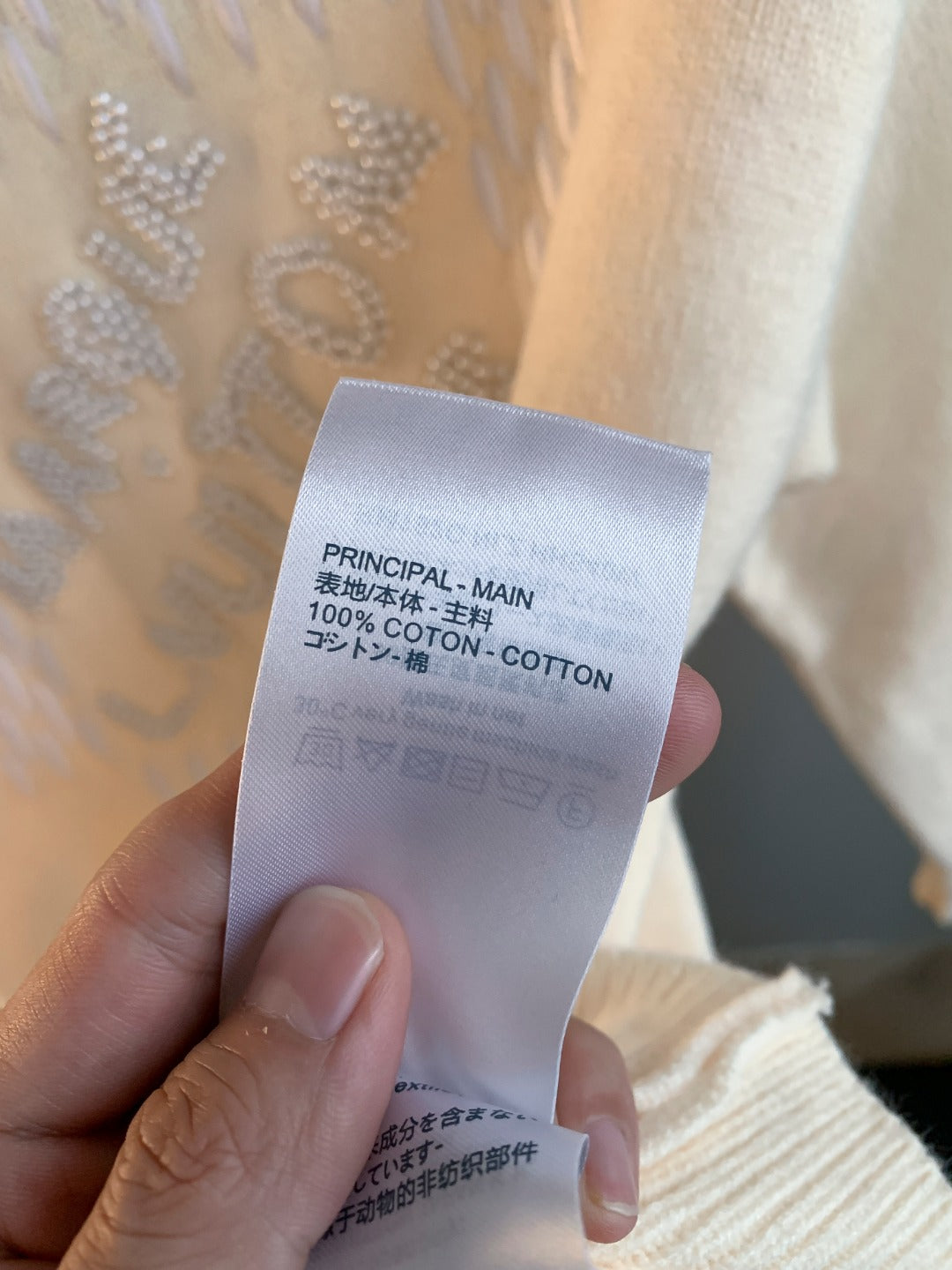 Fabric label showing 100% cotton on a cream knit sweater with rhinestone logo