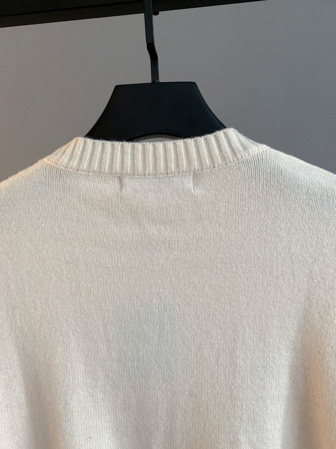 Cream knit crewneck sweater back view with ribbed collar on hanger