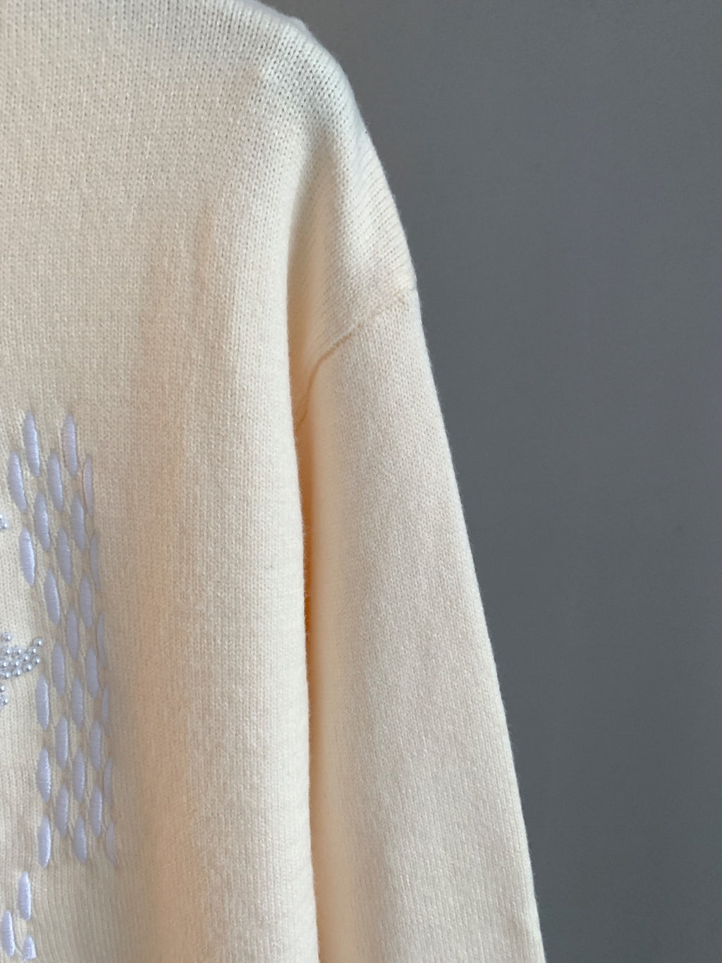 Cream knit sweater sleeve with partial rhinestone logo graphic