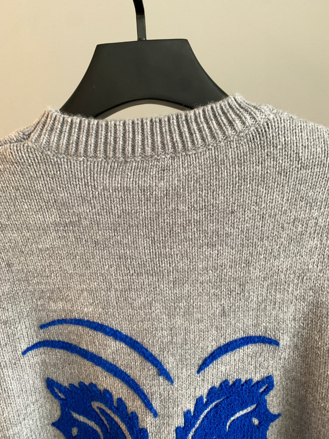 Gray knit sweater close-up of crew neckline with part of blue horse logo on back