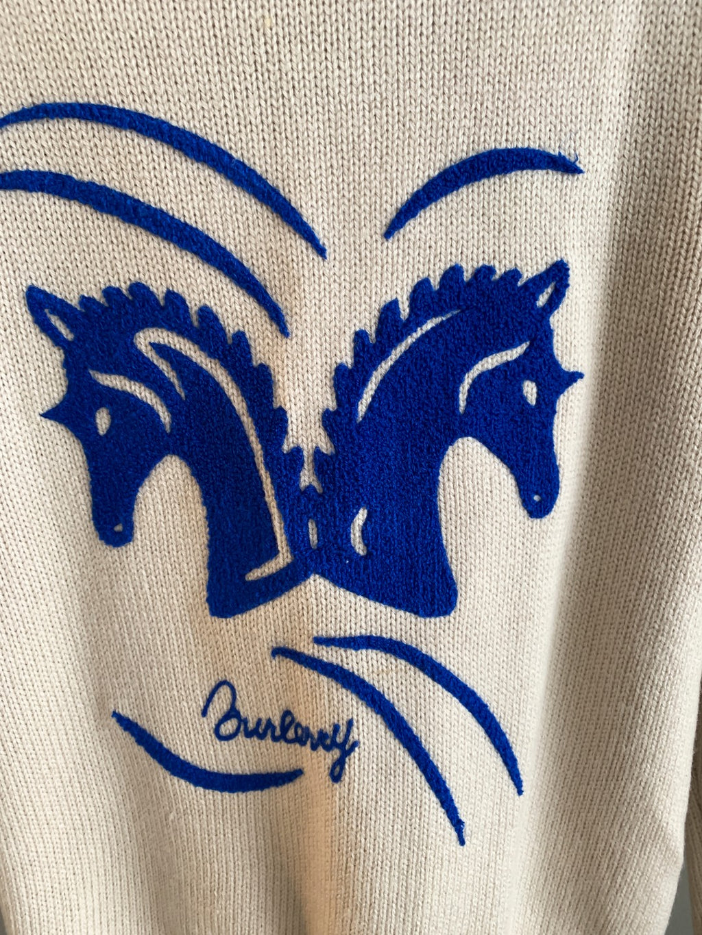 Cream knit sweater with large blue horse heads and arched eye graphic