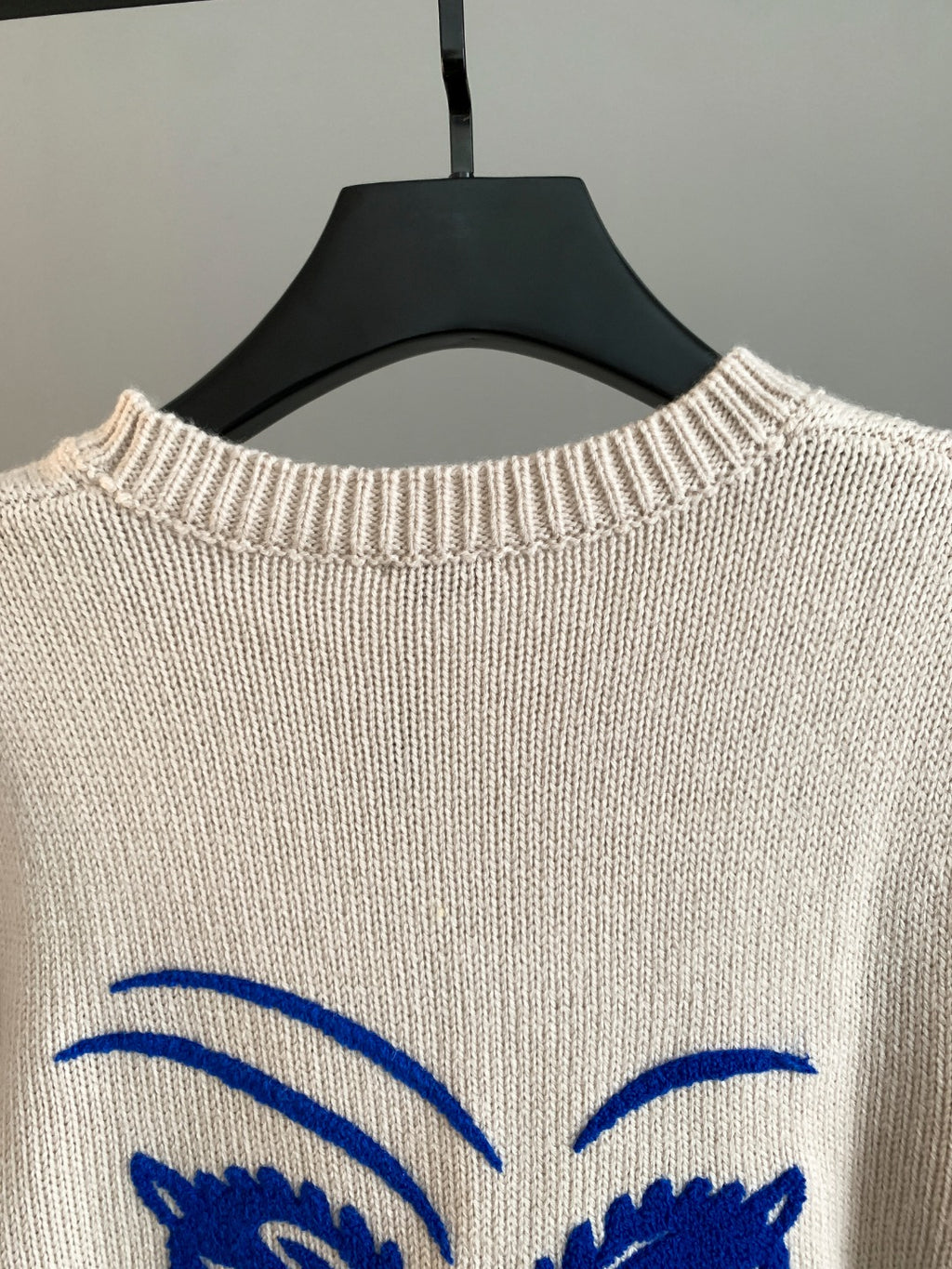 Cream knit sweater with blue arched eyes graphic at upper back