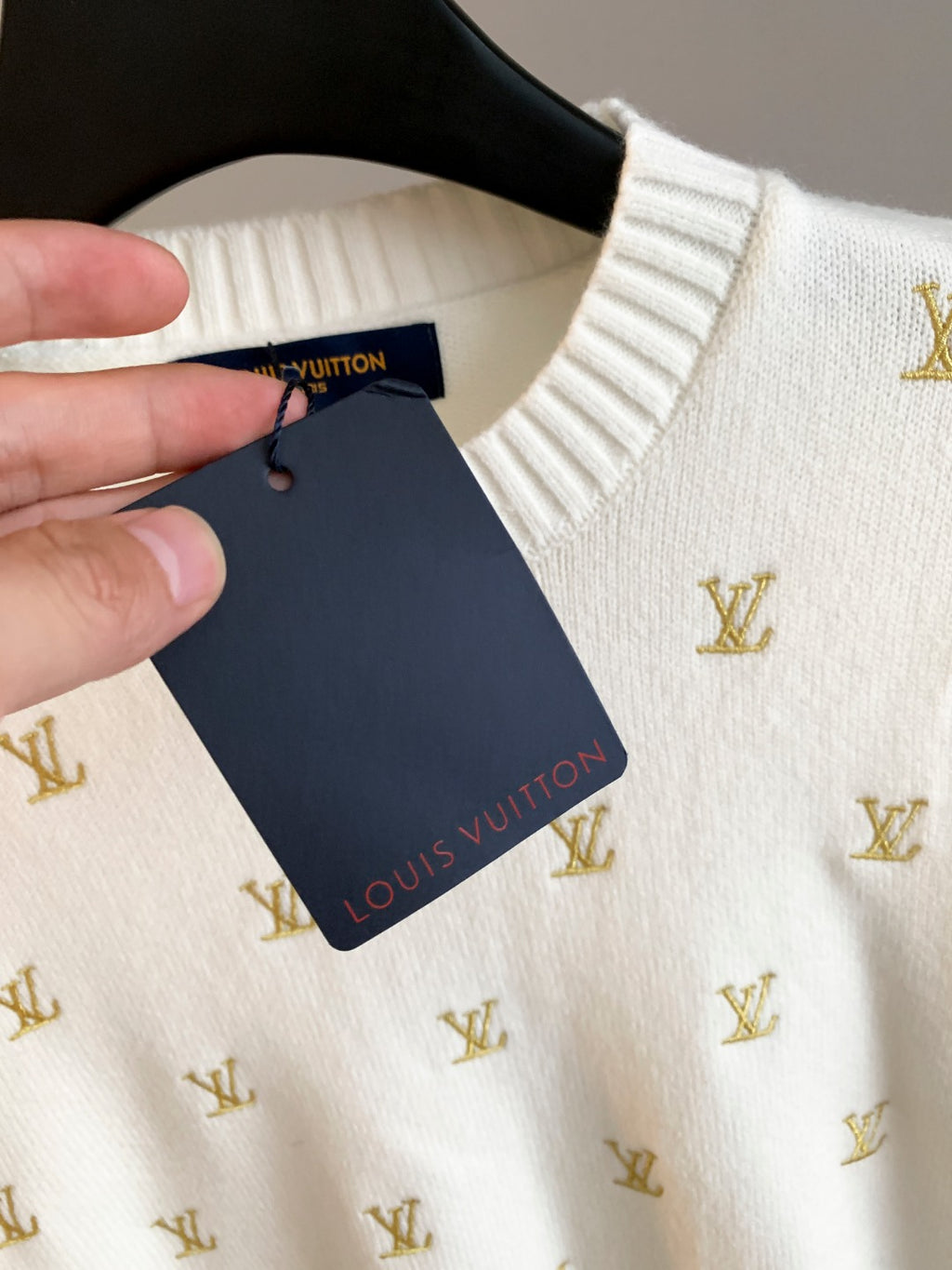 White sweater on hanger with Louis Vuitton hang tag and gold monogram print