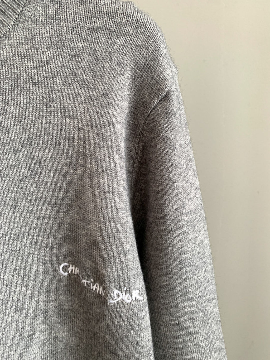 Gray sweater sleeve with small Christian Dior script logo and ribbed knit cuff