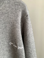 Gray sweater sleeve with small Christian Dior script logo and ribbed knit cuff