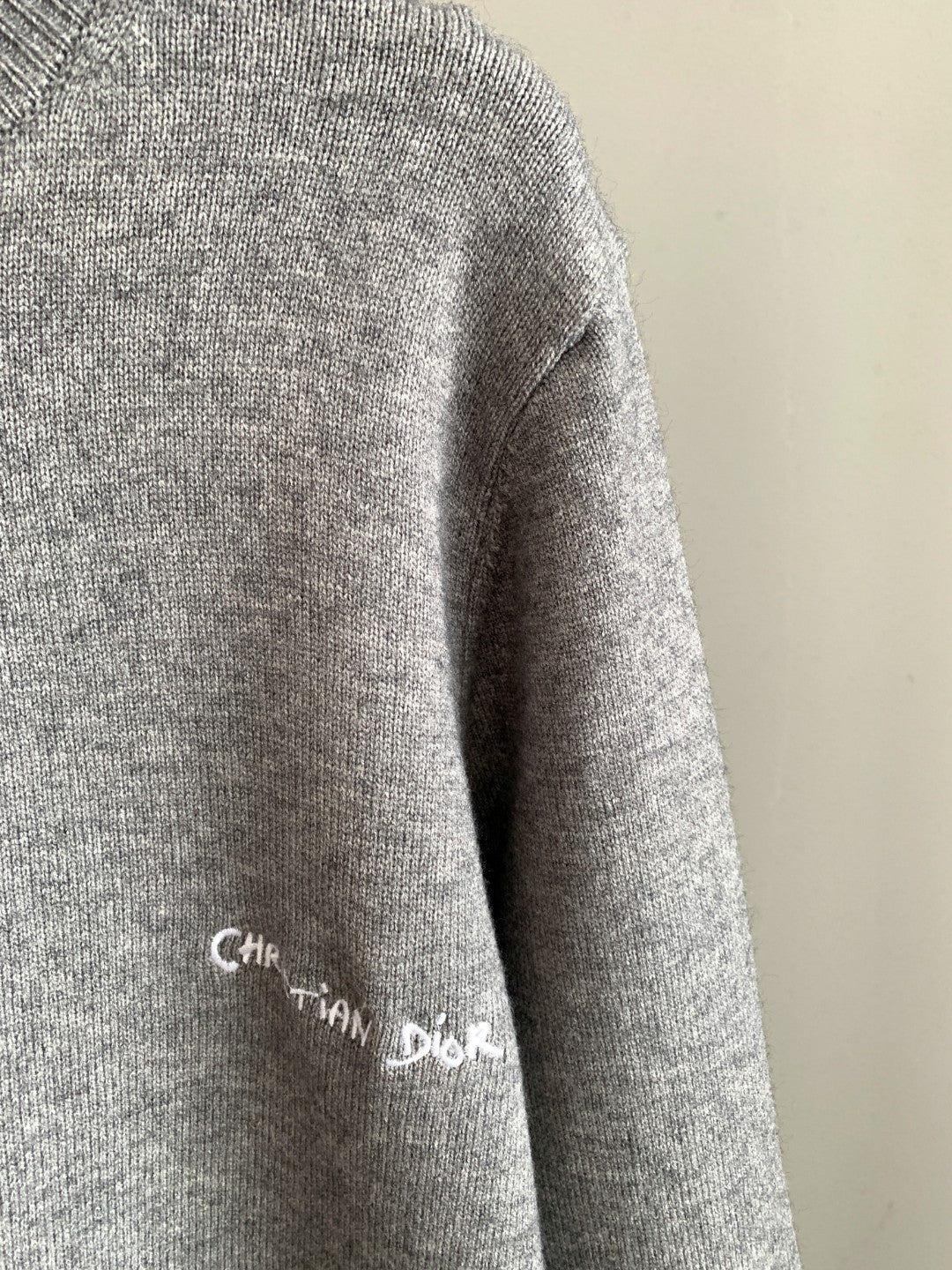 Gray sweater sleeve with small Christian Dior script logo and ribbed knit cuff